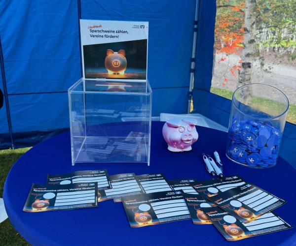 Auf einem Stehtisch mit blauer Husse liegen Gewinnformulare aus, daneben steht ein Plexiglasbriefkasten zum Einwerfen der Formulare.