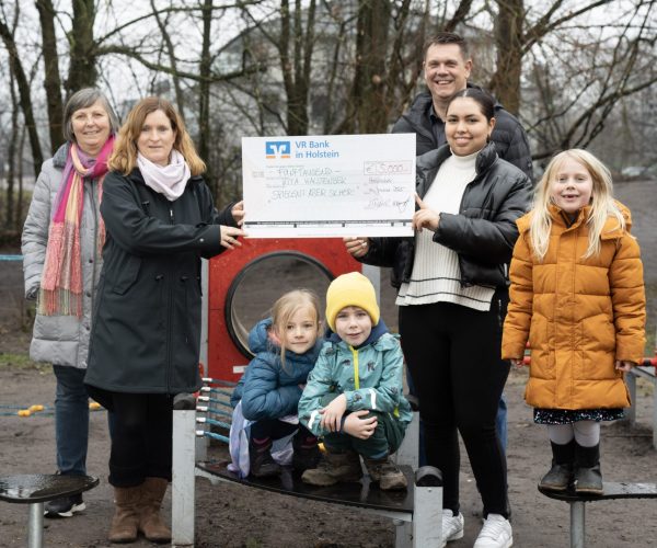 Eine Gruppe von Erzieherinnen ist um ein Spielgerät versammelt und Kindern hält einen riesigen Scheck